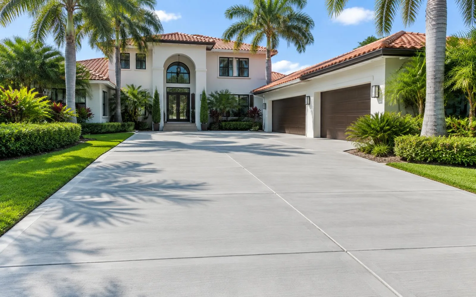 Fresh light-gray broom-finish driveway at a two-story Mediterranean home with palms in Pembroke Pines